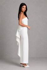 Woman wearing a white strapless jumpsuit with a bow detail on a gray background