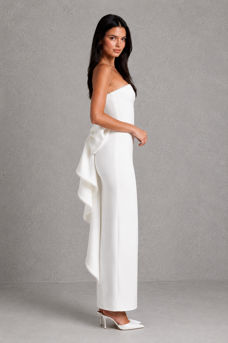 Woman wearing a white strapless jumpsuit with a bow detail on a gray background
