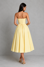 Woman wearing a yellow strapless dress against a gray background