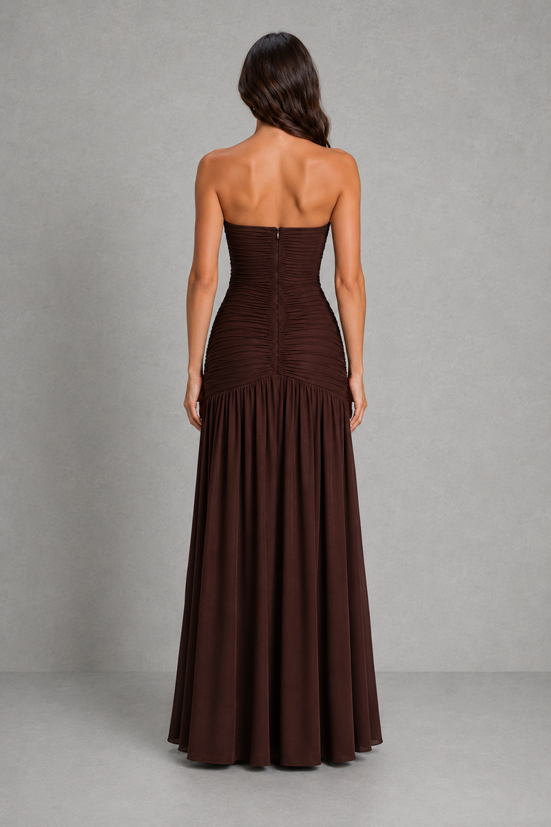 A woman shown from the back wearing a strapless floor-length gown in a very dark brown or near-black color, standing against a plain gray studio backdrop.
