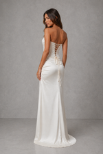 Woman wearing a white strapless gown with lace-up back against a gray background