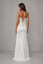 Woman wearing a white strapless gown with lace-up back against a gray background