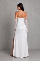 Woman wearing a white strapless gown with sheer sleeves against a gray background