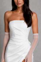 Woman wearing a white strapless dress with sheer gloves against a gray background