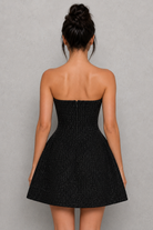 Black strapless dress worn by a model against a gray background