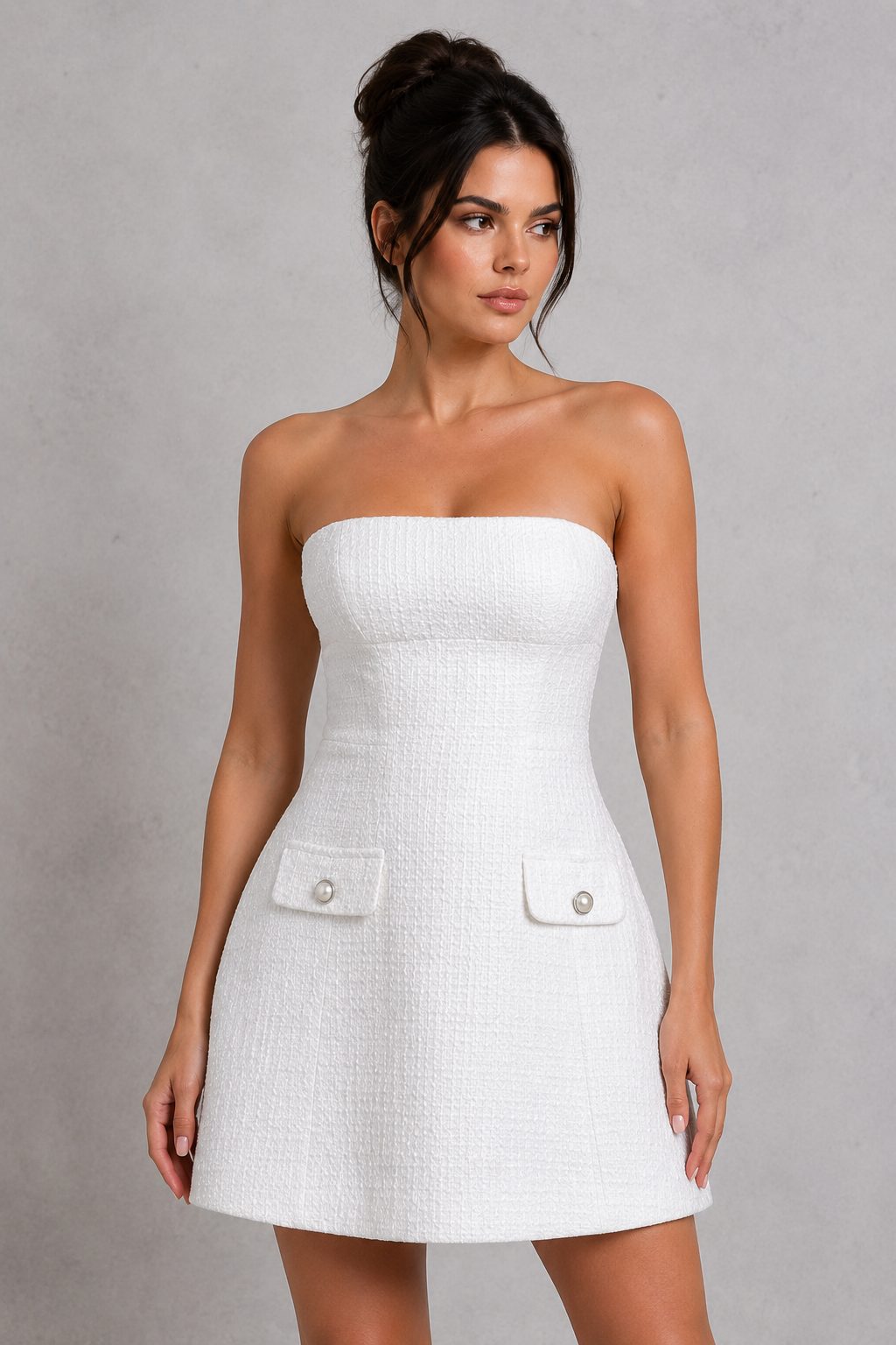 Woman wearing a white strapless dress with button details on a gray background