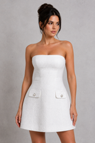 Woman wearing a white strapless dress with button details on a gray background