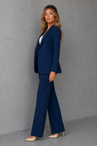 Woman wearing a navy blue suit standing against a gray background