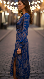 Woman in a blue dress with a pattern standing on a street with blurred lights in the background