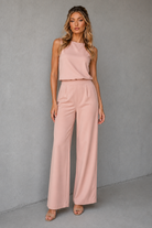 Woman wearing a pink sleeveless top and wide-leg pants against a gray background