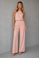Woman wearing a pink sleeveless top and wide-leg pants against a gray background