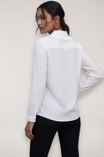 Person wearing a white blouse with long sleeves against a plain background