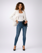 Woman wearing a white blazer, white top, blue jeans, and black heels on a white background