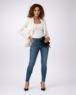 Woman wearing a white blazer, white top, blue jeans, and black heels on a white background