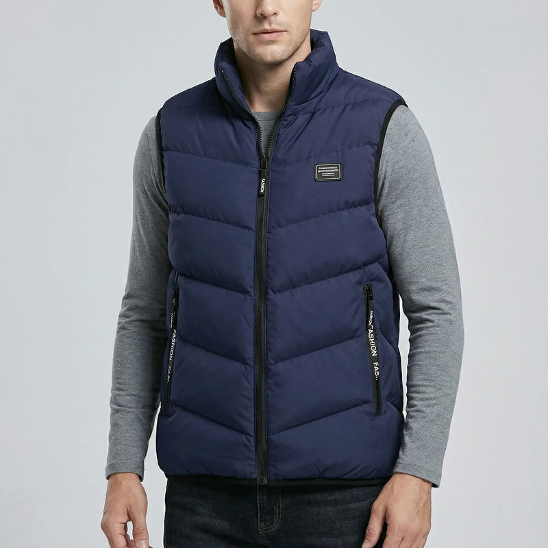 Man wearing a dark blue puffer vest over a gray long-sleeve shirt on a light gray background