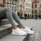 Person wearing white sneakers and light gray jeans sitting on steps in an urban setting.