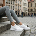 Person wearing white sneakers and light gray jeans sitting on steps in an urban setting.