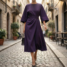 Woman in a purple dress walking down a cobblestone street in an urban setting.