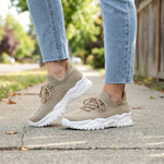 Beige sneakers with white soles worn with light blue jeans on a blurred outdoor background