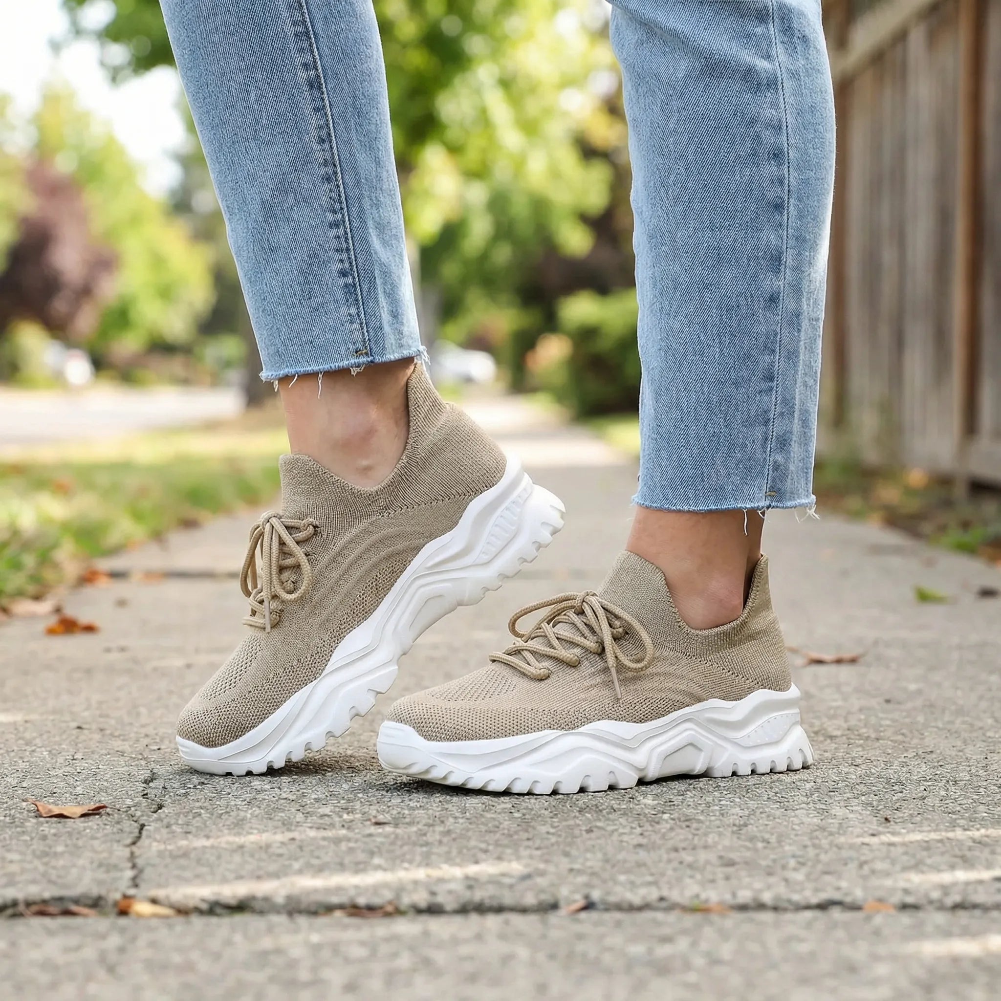 Beige sneakers with white soles worn with light blue jeans on a blurred outdoor background