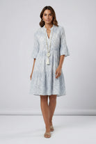 Woman wearing a light blue patterned dress with a white necklace on a plain background1