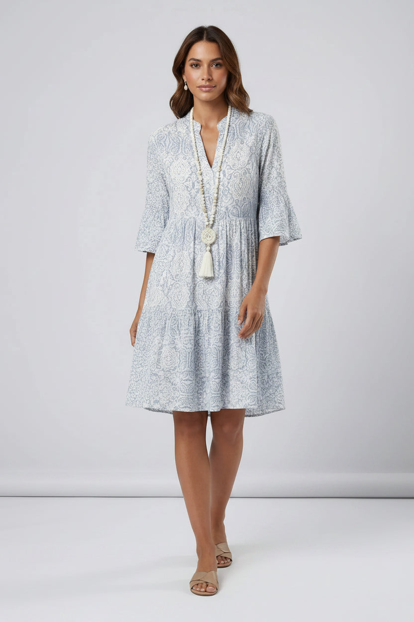 Woman wearing a light blue patterned dress with a white necklace on a plain background1