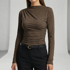 Person wearing a brown long-sleeve top and black pants on a gray background