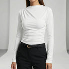 Person wearing a white long-sleeve top and black pants on a light gray background