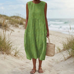 Woman in a green dress standing on a sandy beach with ocean in the background