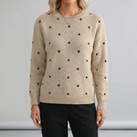 Beige sweater with black polka dots worn by a person on a gray background