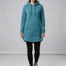 Person wearing a teal hoodie and black leggings on a plain background