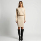 Woman wearing a beige sweater and skirt set with black knee-high boots on a light gray background1