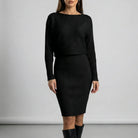 Woman wearing a black ribbed dress against a plain background