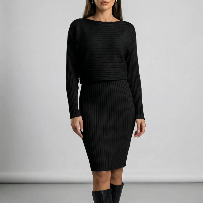 Woman wearing a black ribbed dress against a plain background