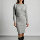 Woman wearing a grey ribbed dress with long sleeves against a plain background