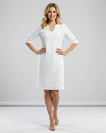 Woman wearing a white dress with a subtle pattern on a plain background