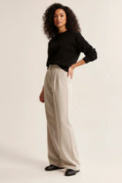 Woman wearing a black sweater and beige pants on a plain background