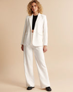 Woman wearing a white suit with a black top against a beige background