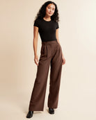 Woman wearing a black top and brown wide-leg pants on a beige background