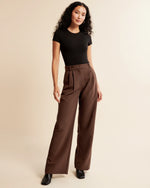 Woman wearing a black top and brown wide-leg pants on a beige background