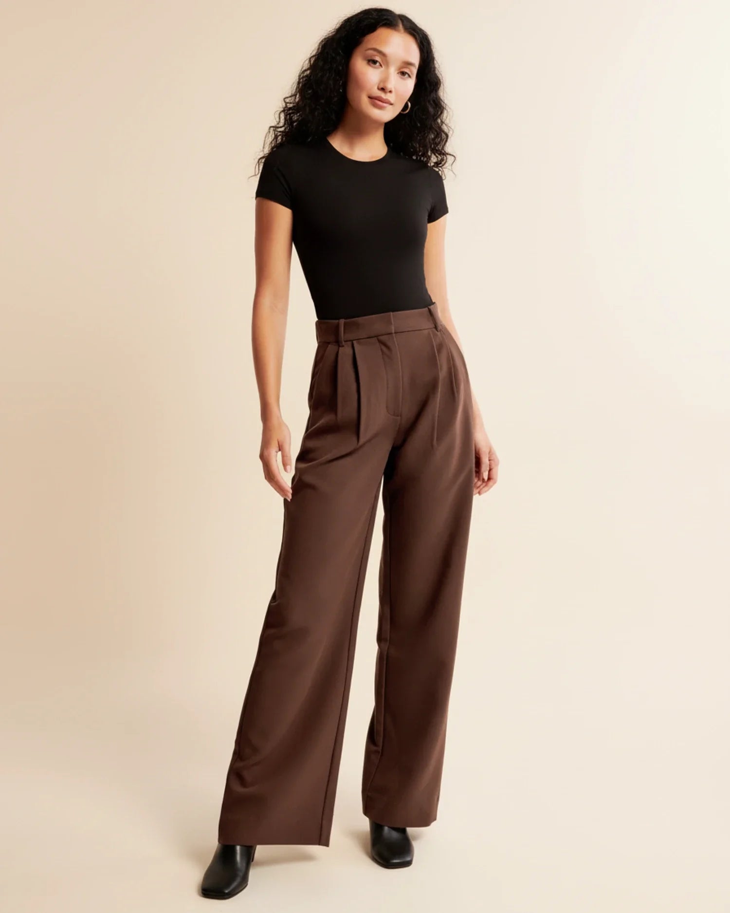 Woman wearing a black top and brown wide-leg pants on a beige background