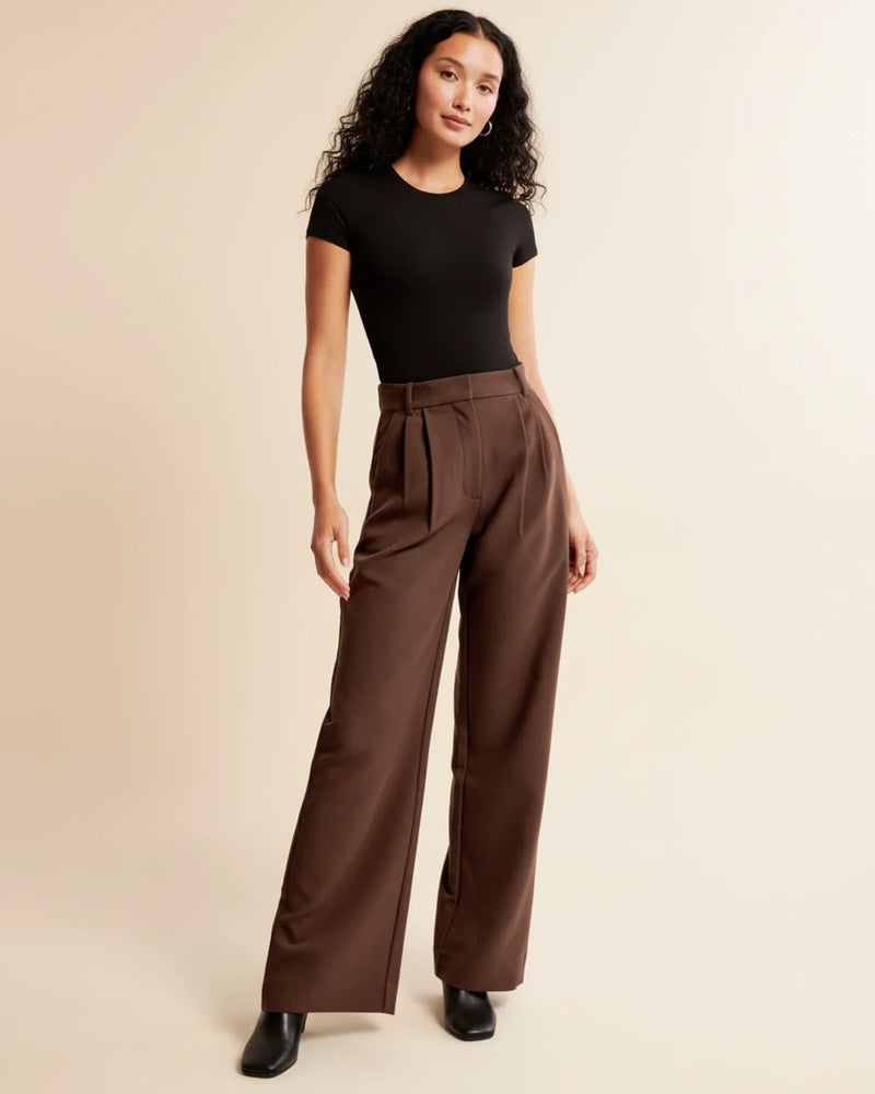 Woman wearing a black top and brown wide-leg pants on a beige background