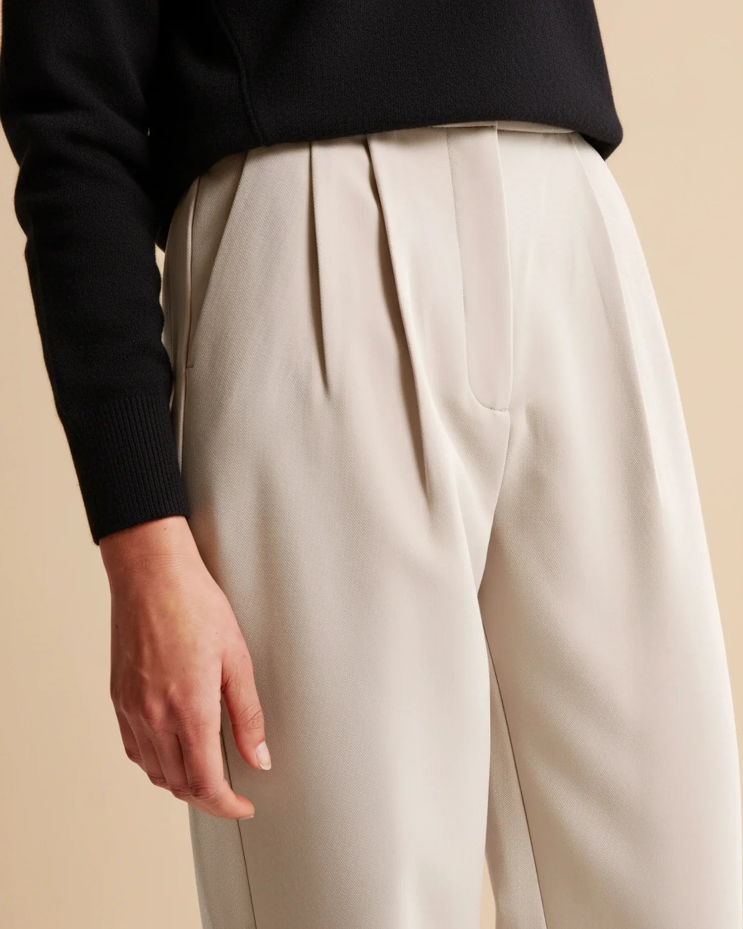 Beige wide-leg pants worn with a black top on a beige background