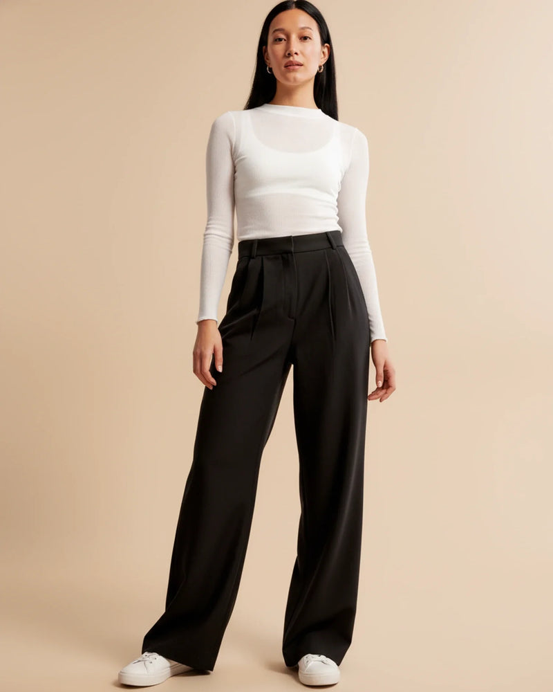 Woman wearing a white long-sleeve top and black wide-leg pants on a beige background