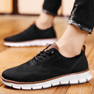 Black athletic shoes with brown accents worn by a person on a wooden floor.