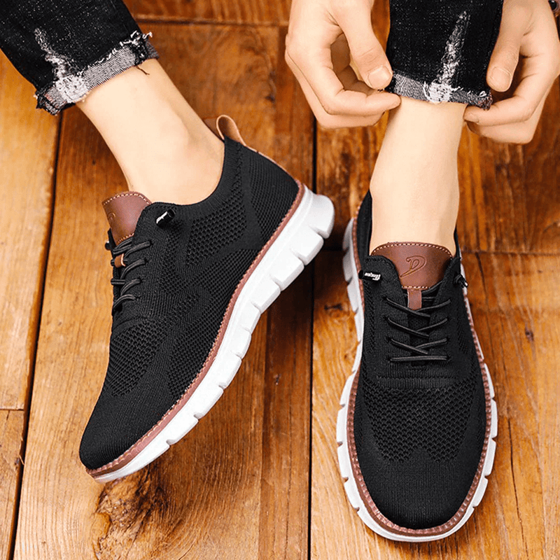 Black sneakers with brown accents worn by a person on a wooden floor