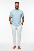 Man wearing a light blue short-sleeve shirt and white pants outdoors.