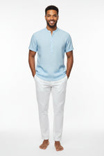 Man wearing a light blue short-sleeve shirt and white pants outdoors.