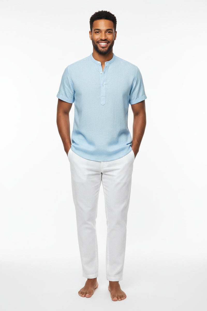 Man wearing a light blue short-sleeve shirt and white pants outdoors.