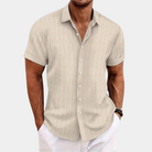Man wearing a beige short-sleeve shirt with white pants on a light gray background